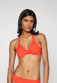 Rød bikini-top med halterneck-design, med en vridd frontdetalj. Glatt tekstur og tettsittende fasong, kombinert med en matchende bunn.