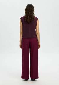 Top senza maniche color bordeaux con vestibilità morbida, abbinato a pantaloni larghi color bordeaux, entrambi caratterizzati da un tessuto liscio e linee pulite.