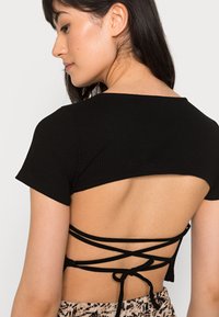 Top preto canelado com mangas curtas e costas abertas com tiras cruzadas amarradas na cintura. Textura suave, design casual.