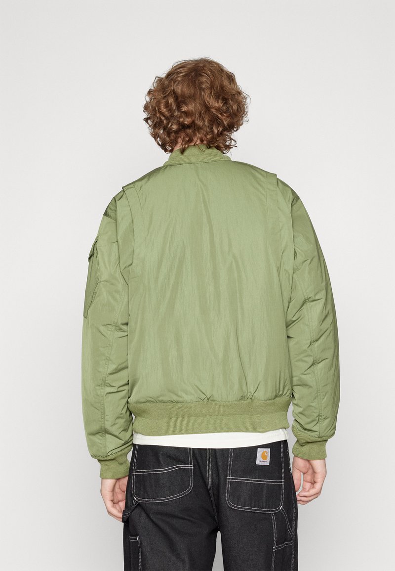Cazadora bomber verde olivo con cierre delantero, cuello y puños acanalados, y un acabado texturizado. Cuenta con bolsillos en los hombros.