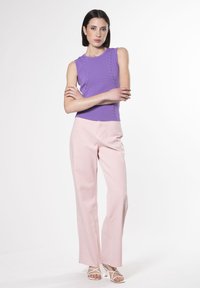 Top viola senza maniche con motivo testurizzato; abbinato a pantaloni dritti rosa chiaro. Sandali con tacco bianchi open-toe.