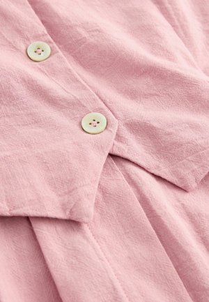 Helle rosa Leinenbluse mit strukturierter Oberfläche, ausgestattet mit zwei runden, cremefarbenen Knöpfen mit jeweils vier Löchern und einem spitzen Kragen.