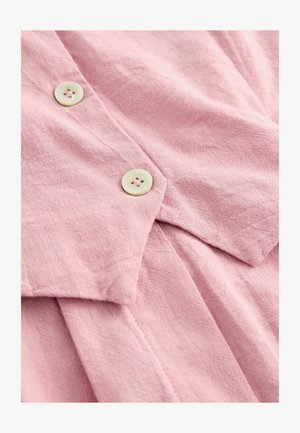 Helle rosa Leinenbluse mit strukturierter Oberfläche, ausgestattet mit zwei runden, cremefarbenen Knöpfen mit jeweils vier Löchern und einem spitzen Kragen.