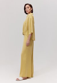 Jasnożółty dwuczęściowy strój składający się z luźnej koszuli z krótkim rękawem oraz spodni z szerokimi nogawkami. Proste białe sandały dopełniają stylizację.