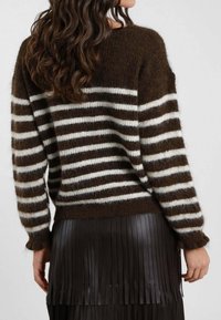 Maglione a righe marroni e crema con una vestibilità ampia e tessuto strutturato, abbinato a una gonna in pelle plissettata nera.