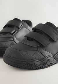 Schwarze Sneakers mit einem strukturierten Design, das ein reptilienähnliches Muster an der Zehe und Dinosauriergrafiken an der Sohle aufweist. Mit Klettverschluss.