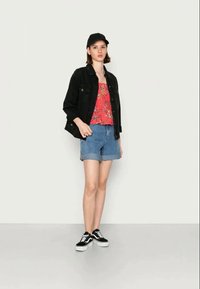 Jaqueta de ganga preta, blusa floral vermelha, calções de ganga azul clara, boné preto e ténis pretos. Design simples, ajuste casual, calções enrolados.