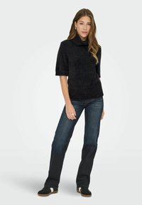 Suéter negro de punto con cuello alto y mangas cortas; combinado con jeans azul oscuro y zapatillas negras con rayas blancas.