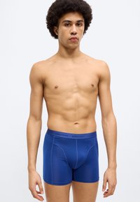 Μπλε μποξεράκια με λεία, ελαστική υφή. Διαθέτουν ελαστική μέση με λογότυπο και εφαρμοστό σχέδιο που αναδεικνύει το σχήμα.