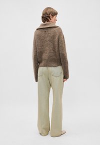 Pulôver castanho fofinho com um colarinho largo, emparelhado com jeans de perna larga em verde claro. O pulôver tem um pequeno detalhe nas costas.