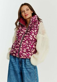 Živá fialová péřová vesta s abstraktními světle růžovými vzory. Vysoký límec, zip vpředu a boční kapsy. V kombinaci s oversized načechranými bílými rukávy.