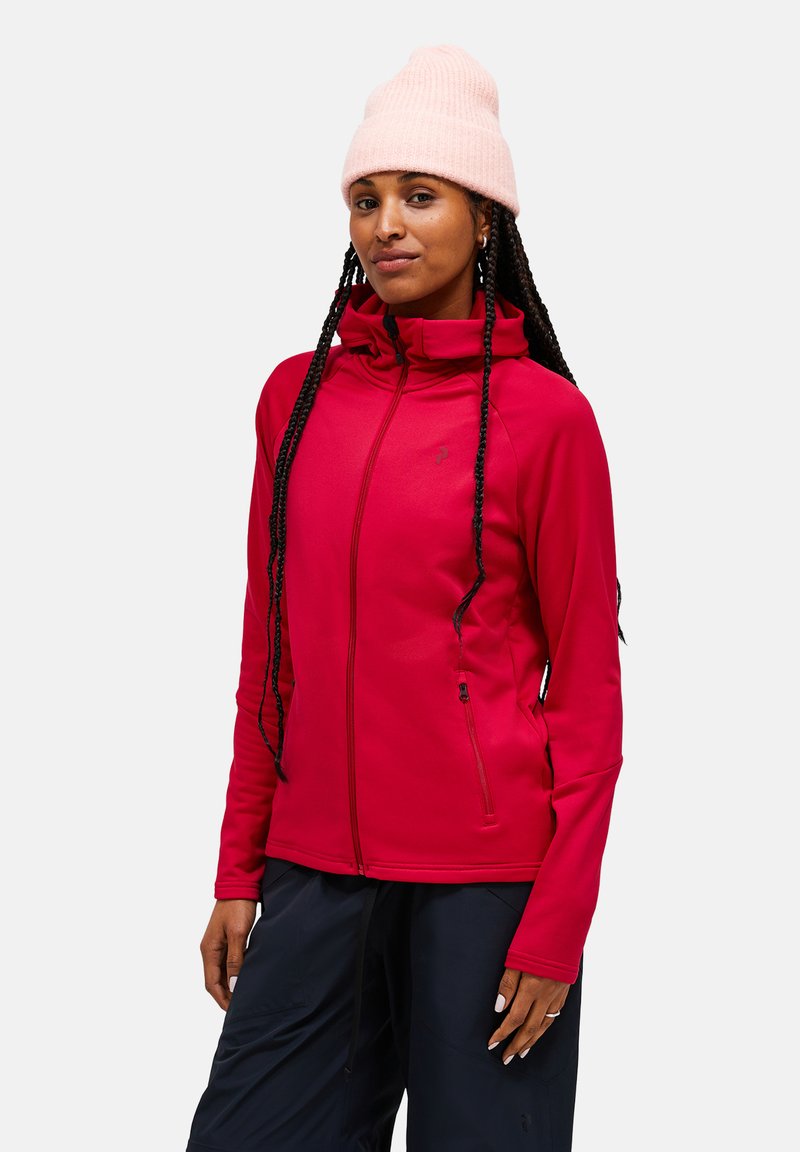 Rode zip-up jack met hoge kraag, gemaakt van rekbare stof. Voorzien van twee ritszakken aan de zijkanten en een slim fit ontwerp. Gedragen met een roze beanie.
