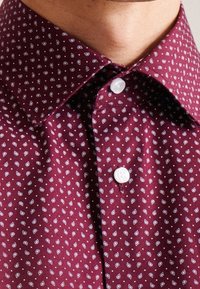 Burgundské košile s vzorem a límcem na knoflíky, zdobené malým bílým listovým motivem, texturovanou tkaninou a bílými plastovými knoflíky.