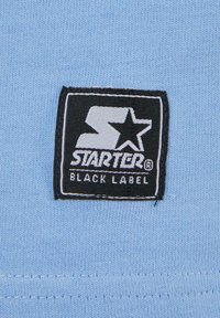 Light blue fabric with a textured surface features a black rectangular label displaying a white logo and "STARTER BLACK LABEL" text.