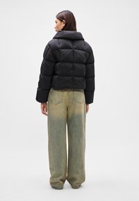 Doudoune noire au design court, avec un col haut, une texture matelassée et des manches légèrement oversize, associée à un pantalon en denim clair.
