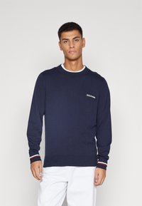 Maglione lavorato a maglia di colore blu navy con maniche lunghe, scollo rotondo e orlo a coste. Presenta un logo a contrasto sul petto e dettagli a righe sui polsini.