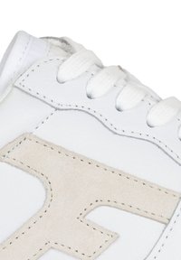 Sneaker in pelle bianca con un morbido logo in suede beige, lacci bianchi piatti, cuciture curve e una superficie liscia e texture.