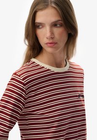Rood en wit gestreepte long-sleeve shirt met een ronde hals en een klein geborduurd detail op de borst. Zacht katoen materiaal en een ontspannen pasvorm.