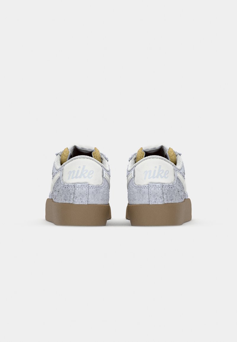 Baskets Nike avec un dessus en daim gris, des accents blancs et une semelle en caoutchouc marron. Équipées d'un col rembourré et d'un logo détaillé sur le talon.