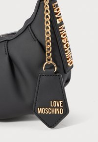 Black leather handbag with gold chain strap and "LOVE MOSCHINO" gold lettering on a leather tag and along the edge.