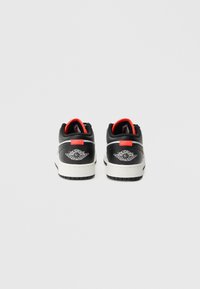 Μαύρα και γκρι δερμάτινα αθλητικά παπούτσια με λευκές λαστιχένιες σόλες. Κόκκινες λεπτομέρειες στο πίσω μέρος και στη γλώσσα, με λογότυπο σε κάθε φτέρνα.