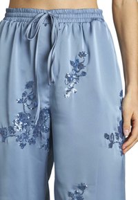 Lichtblauwe satijnen broek met elastische tailleband en trekkoord, voorzien van blauwe pailletten bloemenborduursels. Casual ontwerp, losse pasvorm.