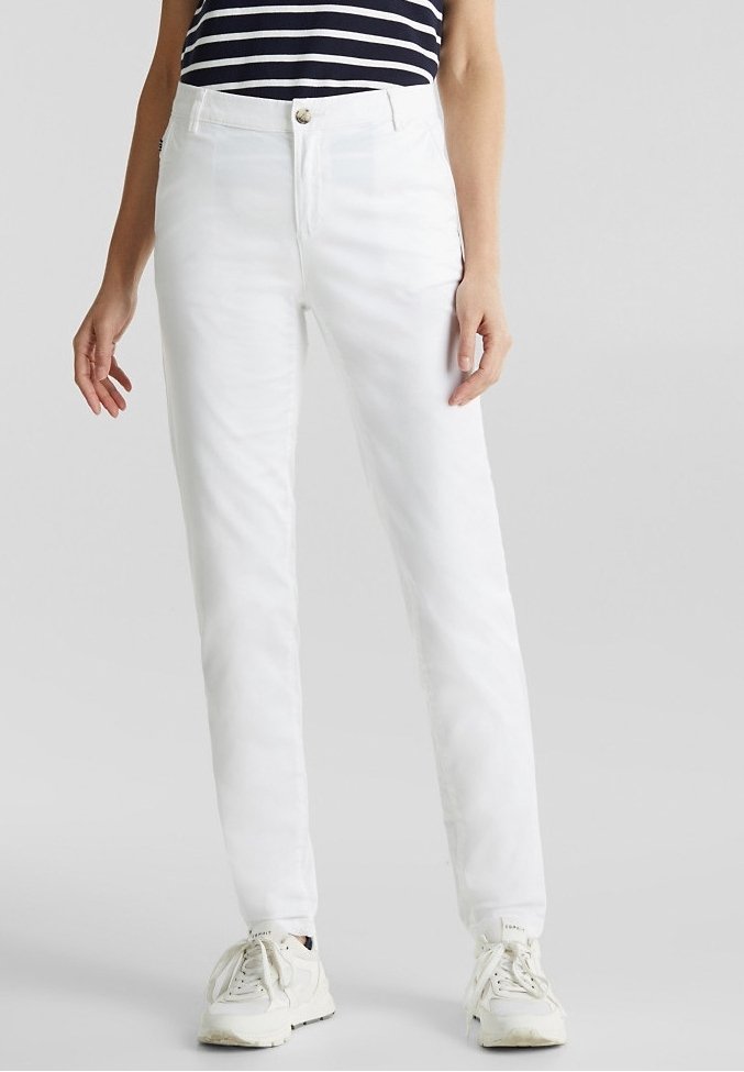 Pantalon en mélange de coton blanc à coupe slim, doté d'une braguette zippée et d'une fermeture à bouton. Associé à des baskets blanches, présenté sur un fond neutre.