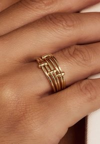 Goldfarbene Metallringe mit eleganten, abgerundeten Designs in unterschiedlichen Breiten und glatten Oberflächen, übereinander gestapelt auf einer Hand.