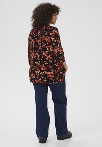 Blusa negra con estampado floral rojo, de manga larga, con escote fruncido; combinada con jeans acampanados azules y zapatos de plataforma negros.