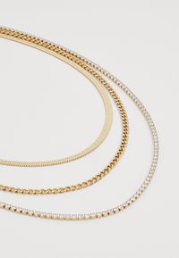 Three golden necklaces: a flat herringbone chain, a classic curb chain, and a shiny chain with clear rhinestones along the edge.