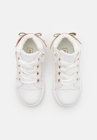 Hvite ankelhøye sneakers med gyldne snørehull, hvite snører og brune detaljer. Mykt, teksturert materiale med rund tå og dekorative sløyfer.