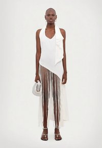 Balta asimetrinė suknelė su raukšlėtu apykakle, kutais puošta apačia ir permatomu audiniu, derinama su sidabrine delninuke ir dirželiais aplietais sandalais.