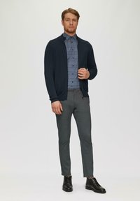 Granatowy kardigan na niebieskiej koszuli w kratę z guzikami, szare spodnie slim-fit oraz czarne skórzane buty. Gładkie tekstury i dopasowany krój.
