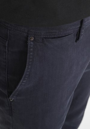 Pantaloni in cotone blu navy con zip, dotati di un piccolo bottone metallico, passanti per cintura e una finitura in tessuto testurizzato.