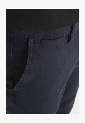 Pantaloni in cotone blu navy con zip, dotati di un piccolo bottone metallico, passanti per cintura e una finitura in tessuto testurizzato.