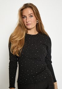 Musta pitkähihaista toppia, jossa on ribbikuvio ja pieniä valkoisia pistekuvioita. Pyöreä pääntie ja hieman rispaantunut helma alareunassa.