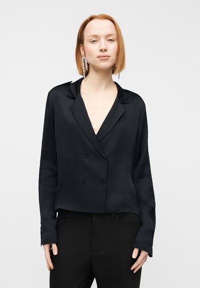 Μαύρο διπλό περπάτητο σατέν σακάκι με γιακά με αυλάκι, κοντό μήκος και μακριά μανίκια, συνδυασμένο με μαύρο παντελόνι για μονοχρωματική εμφάνιση.