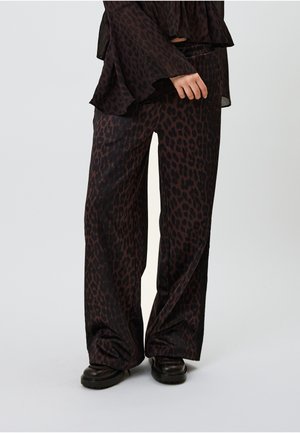 Pantalon large en tissu foncé avec un motif léopard marron. Texture lisse, taille élastique, associé à des chaussures noires.