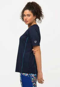Camiseta atlética de color navy con mangas cortas, que presenta un cuello redondo, líneas de acento en turquesa a los lados y un logo en la manga izquierda.