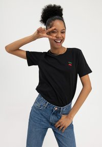 T-shirt en coton noir à manches courtes avec une illustration de cerise sur la poitrine, associé à un jean en denim bleu taille haute.