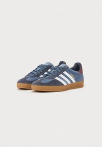 Zapatillas de ante azul con rayas y acentos blancos, suela de goma, parte superior texturizada, diseño de cordones y detalles del logo en el lateral y la lengüeta.