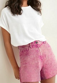 Hvid tekstureret kortærmet top parret med pink højtaljede denimshorts. Shortsene har et falmet design og rå kantdetaljer.