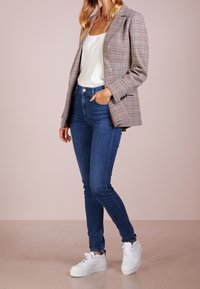 Saka s houndstooth vzorem v béžové a hnědé, spárované s bílým saténovým topem, modrými skinny džíny a bílými platformovými teniskami.