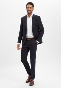 Marineblauer Anzug mit maßgeschneiderter Passform, kombiniert mit einem weißen Hemd. Brauner Ledergürtel und passende Schuhe vervollständigen den Look. Glatter Stoff mit klaren Linien.