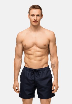 Marineblaue Badeshorts mit einem elastischen Taillenbund und verstellbarem Kordelzug. Das Material wirkt leicht und glatt, mit einer lockeren Passform.