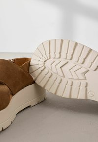 Sandal in suede marrone con una suola in gomma cremosa e chunky, caratterizzata da un motivo di battistrada testurizzato, vista angolata che mostra i dettagli esterni e della suola.