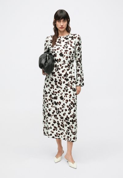 Maxi šaty v bielej farbe s čiernym a hnedým kvetinovým vzorom; dlhé rukávy; splývavá látka; doplnené čiernou taškou a svetlými balerínami.