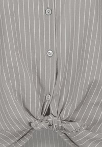Gray striped shirt with white vertical lines, featuring a button-up front and a knotted detail at the hem. Fabric appears lightweight.