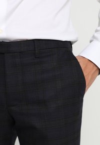 Marinblå rutiga byxor tillverkade i en strukturerad tyg, med flat front, sidofickor och en slim fit-design.
