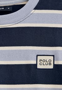 Navyblå och ljusgrå randig T-shirt med rundad halsringning och en fyrkantig etikett som säger "POLO CLUB" i nedre vänstra hörnet.